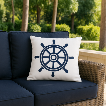 White pillow with a navy blue ship's wheel design on a navy blue outdoor sofa with a green garden background.
